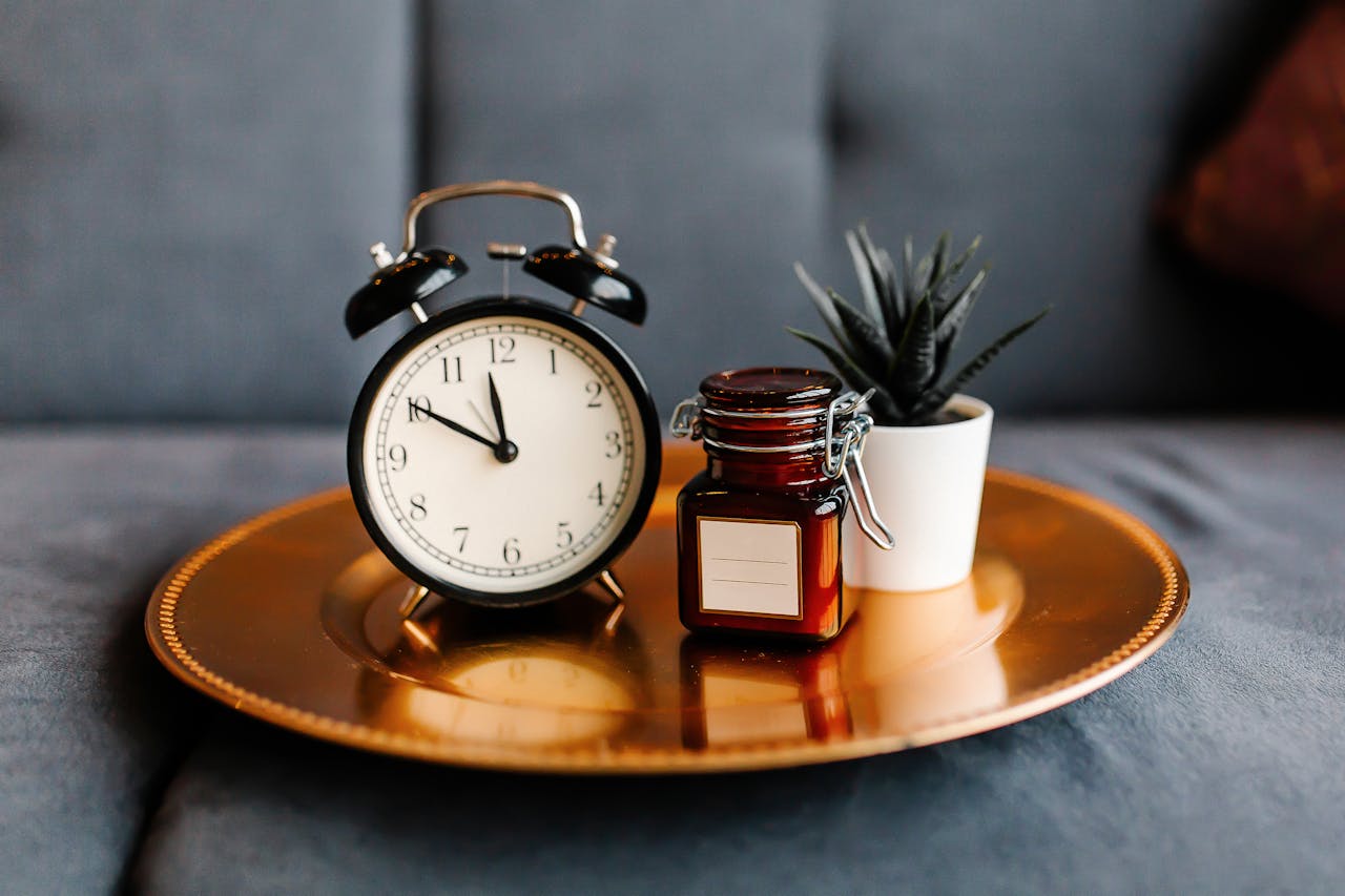Aesthetic arrangement of a clock and jar on a golden tray with a potted plant.